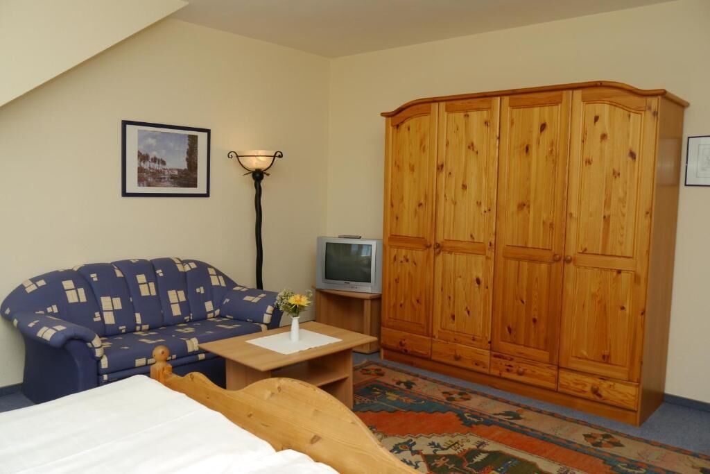 Una habitación con cama, sofá azul, armario de madera, televisor y lámpara.