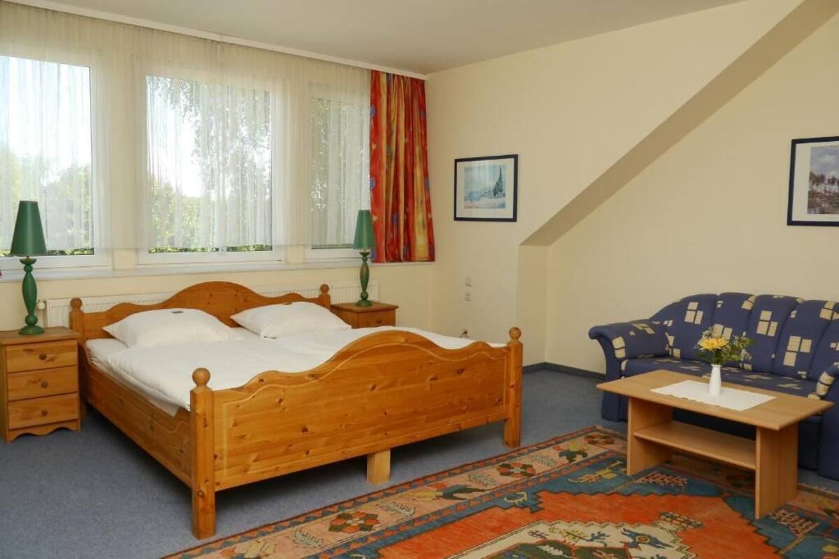 A bedroom with a wooden bed, a blue sofa, a small table, and a patterned rug.