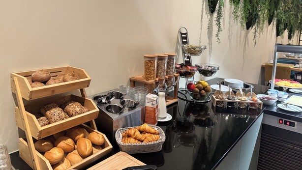 A buffet setup with various food items, including bread, pastries, and fruits. - Erbenholz Hotel (Laatzen)