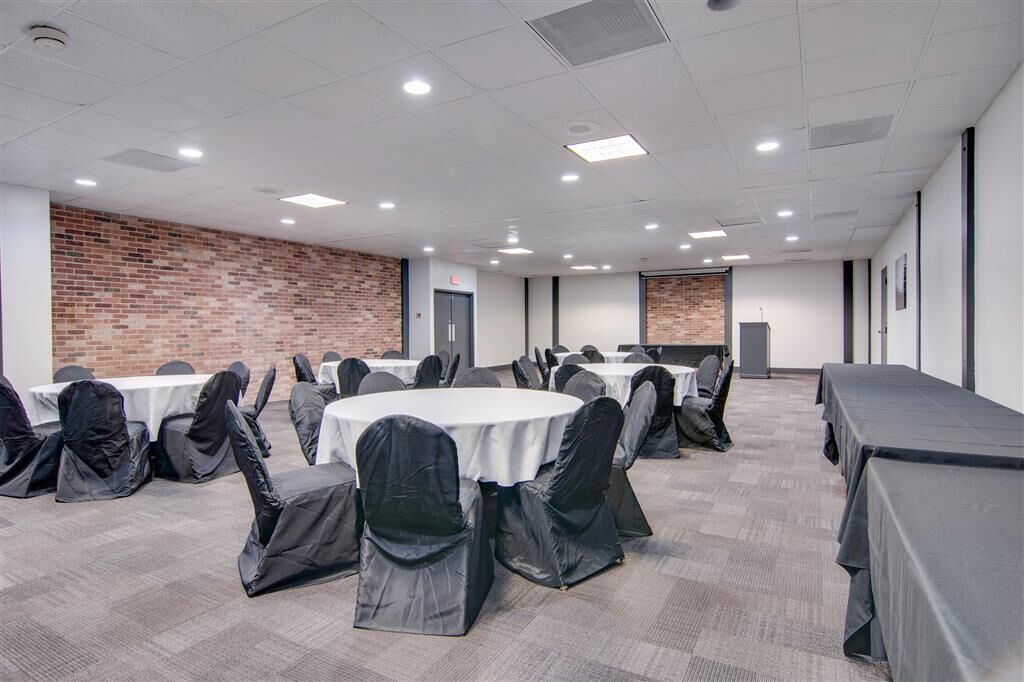 A conference room with round tables and chairs, a brick wall, and a long table covered with a tablecloth.