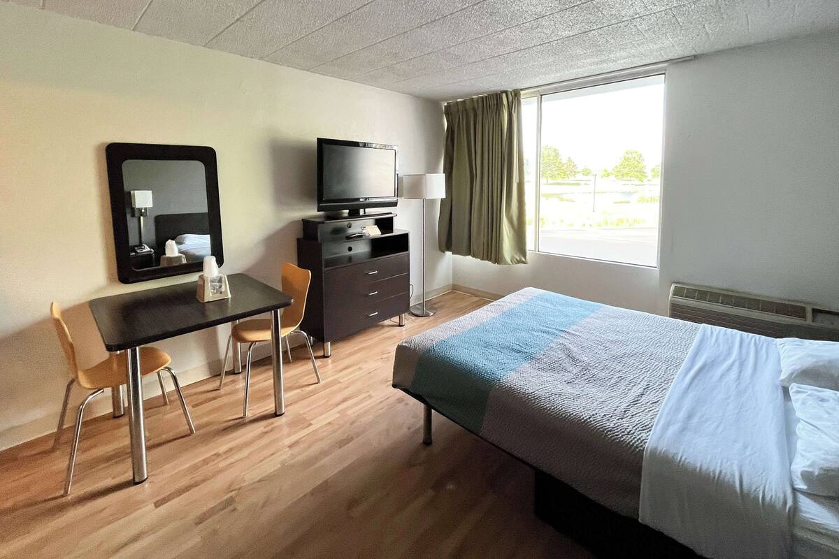 A hotel room with a bed, a desk, a chair, a television, and a window with curtains.
