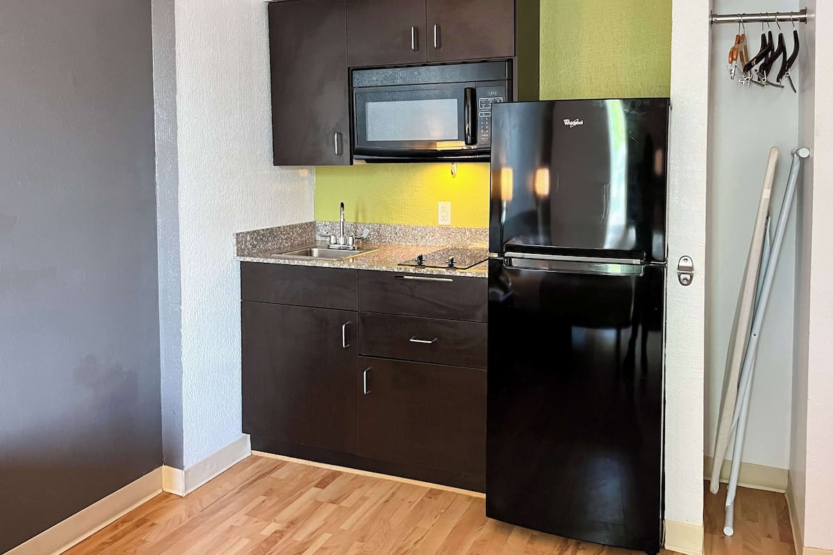 A compact kitchen with dark cabinets, a stainless steel refrigerator, a microwave, and a sink.