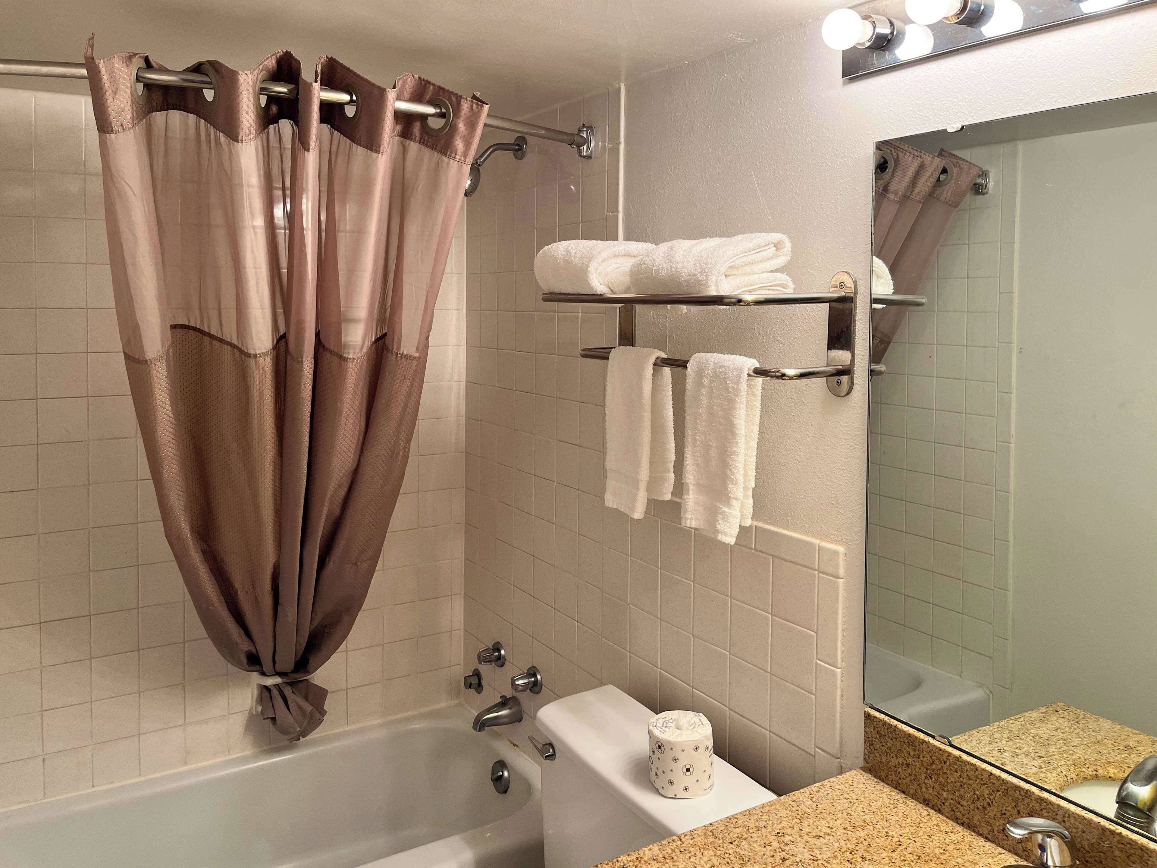 A bathroom with a bathtub, a toilet, a towel rack with towels, a shower curtain, and a mirror.