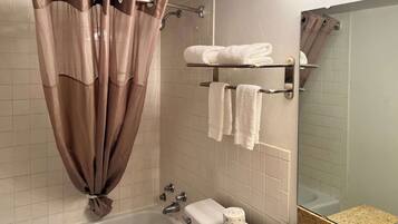 A bathroom with a bathtub, a toilet, a towel rack with towels, a shower curtain, and a mirror.