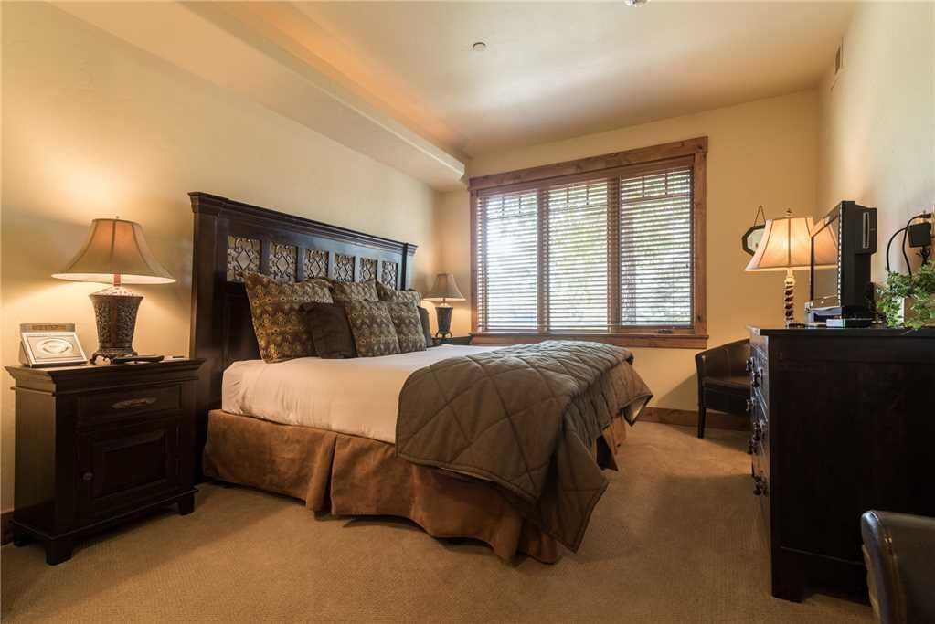 A bedroom with a large bed, two bedside tables, a dresser, and a window with blinds.