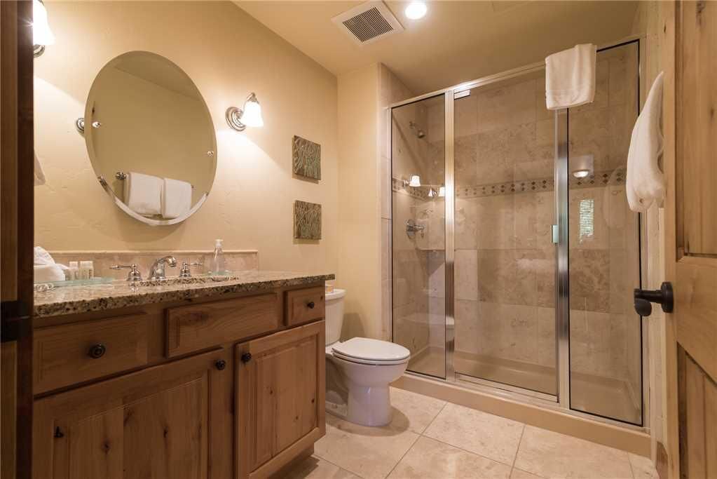 Un baño con tocador de madera, espejo redondo, inodoro y zona de ducha con mampara de cristal.