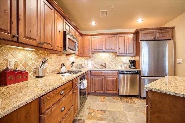 A kitchen with wooden cabinets, granite countertops, stainless steel appliances, and a tiled backsplash. - 5114 Emerald Lodge, Trappeur's Crossing Apartment 1 (Steamboat Springs)