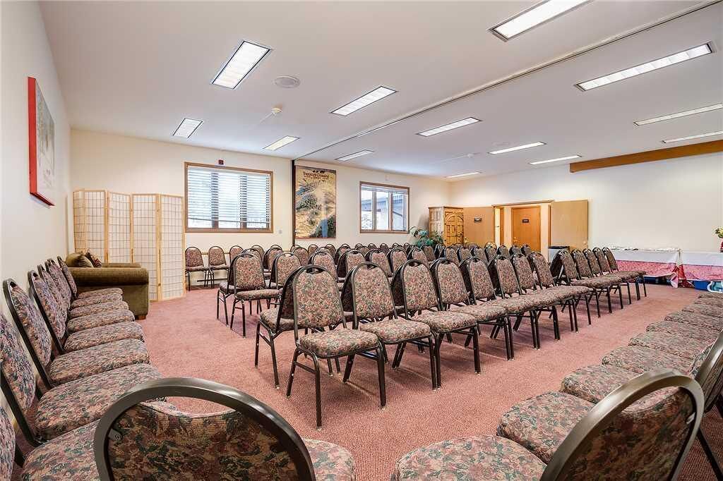 A conference room with rows of chairs, a carpeted floor, and a ceiling with rectangular lights.