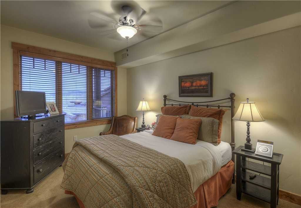A bedroom with a bed, a dresser, a ceiling fan, and a window with blinds.