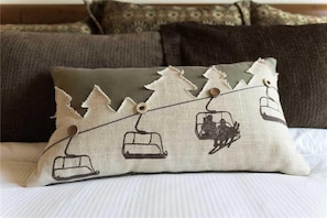 A pillow with a ski lift design, placed on a bed with a white comforter. - 5203 Emerald Lodge, Trappeur's Crossing Apartment 4 (Steamboat Springs)
