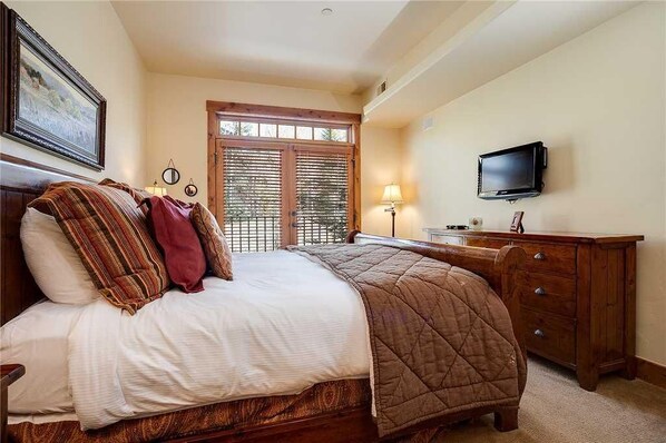 A bedroom with a large bed, a wooden dresser, a television, and a window with shutters.