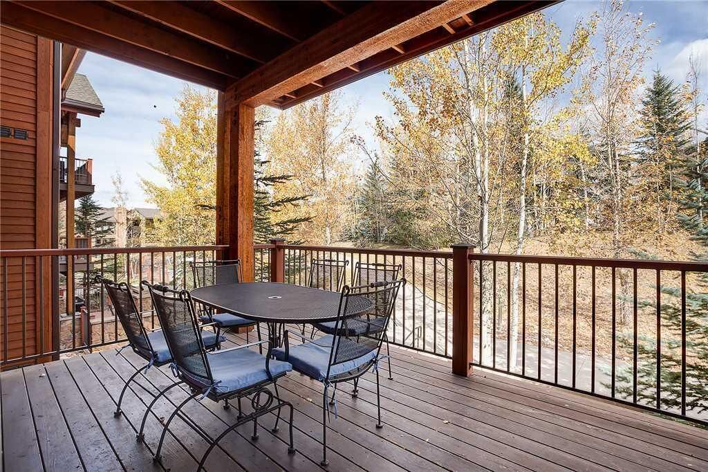 A wooden deck with a table and chairs, overlooking a forested area.