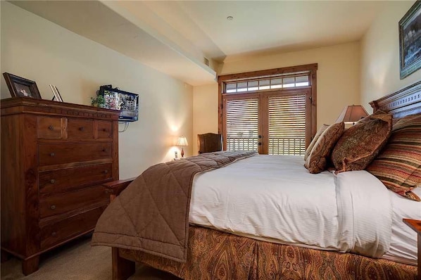 A bedroom with a bed, wooden dresser, and a window with blinds.