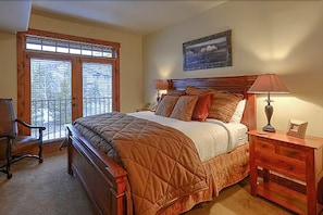 A bedroom with a large bed, a wooden nightstand, a chair, and a window with blinds.