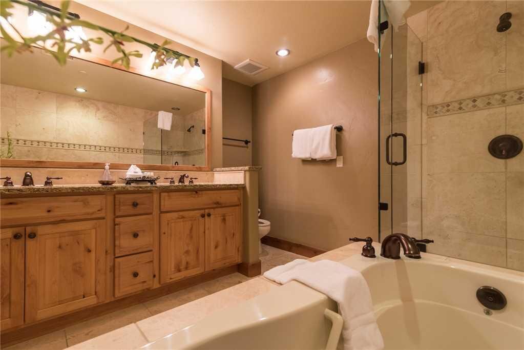 A bathroom with a wooden vanity, a large mirror, a bathtub, and a shower area.