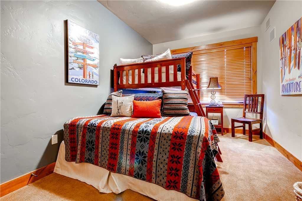 A bedroom with a bunk bed, a desk, a chair, and a window with blinds.