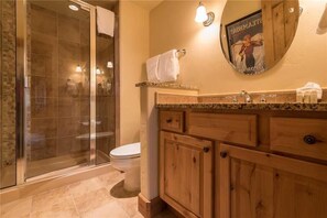 A bathroom with a glass shower enclosure, a toilet, wooden cabinets, and a towel rack.