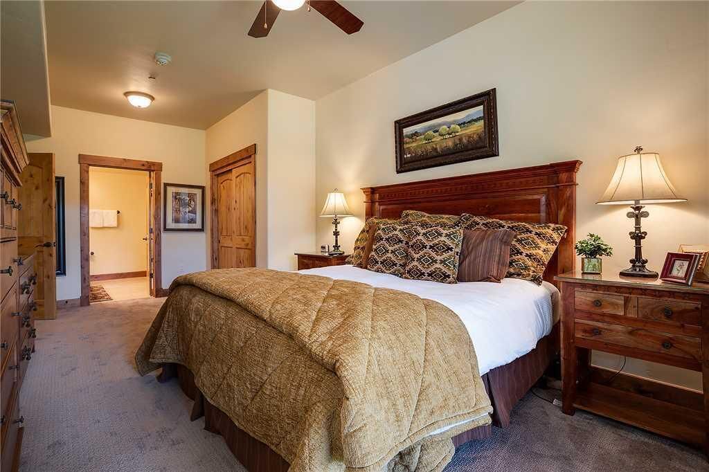 A bedroom with a large bed, wooden headboard, two bedside tables with lamps, a ceiling fan, and a framed picture on the wall.