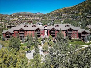 A multi-story lodge with a central courtyard, surrounded by trees and a mountainous backdrop. - 5307 Emerald Lodge, Trappeur's Crossing Apartment 4 (Steamboat Springs)