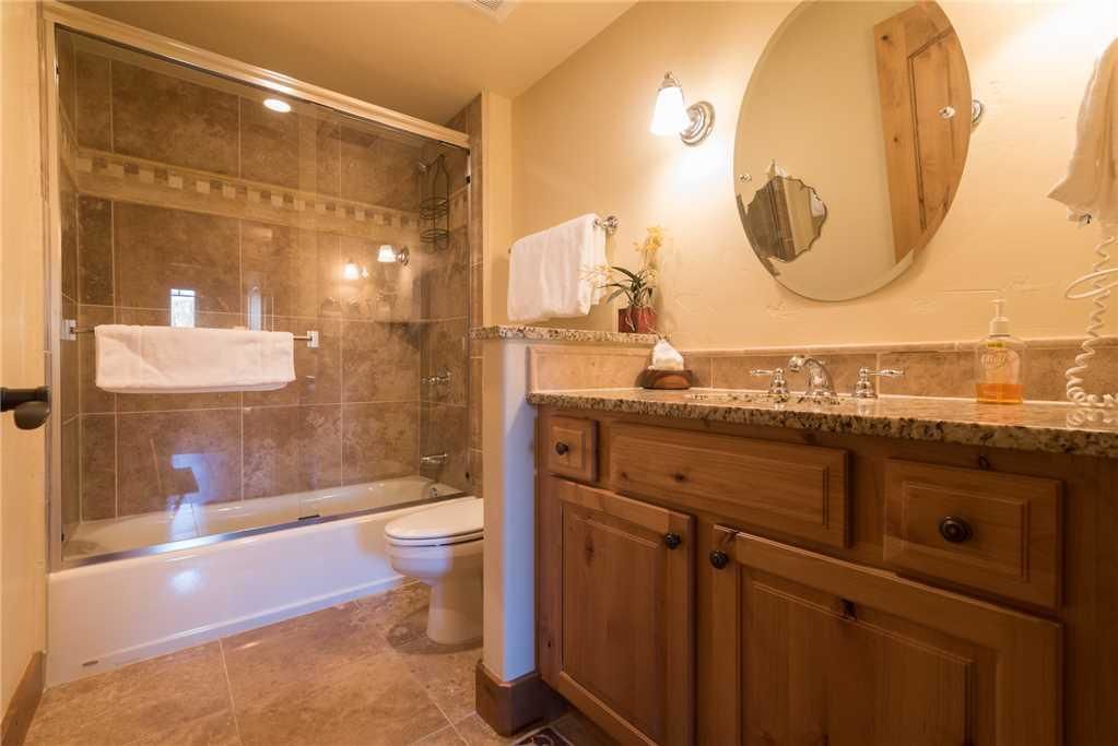 A modern bathroom with a glass-enclosed shower, a bathtub, a toilet, wooden cabinets, and a vanity with a mirror.