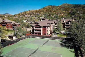 En tennisbana omgiven av byggnader med ett bergigt landskap i bakgrunden.