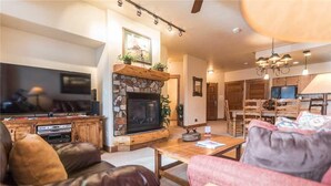 A cozy living room with a stone fireplace, a television, and comfortable seating. - 2101 Timberline Lodge, Trappeur's Crossing Apartment 2 (Steamboat Springs)