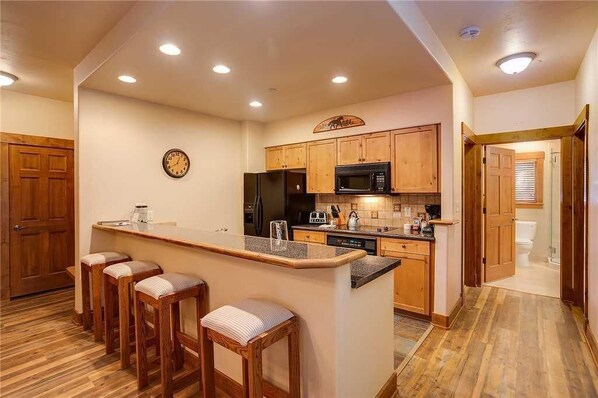 A kitchen with wooden cabinets, a microwave, a refrigerator, and a bar area with stools. - 2103 Timberline Lodge, Trappeur's Crossing Apartment 2 (Steamboat Springs)