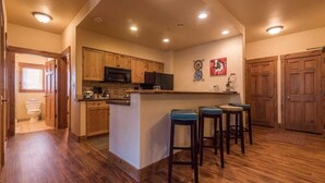 Une cuisine avec des meubles de rangement en bois, un îlot central doté de tabourets et des spots encastrés au plafond.