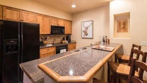 A kitchen with wooden cabinets, a black refrigerator, a microwave, and a granite countertop. - 2106 Timberline Lodge, Trappeur's Crossing Apartment 2 (Steamboat Springs)