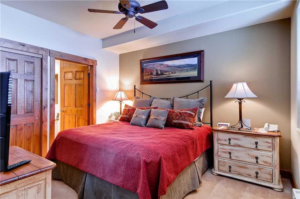 A bedroom with a bed, a television, a dresser, a ceiling fan, and a painting on the wall.