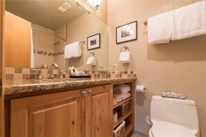 Een badkamer met houten kastjes, een granieten aanrechtblad, een toilet en twee ingelijste foto’s aan de muur.