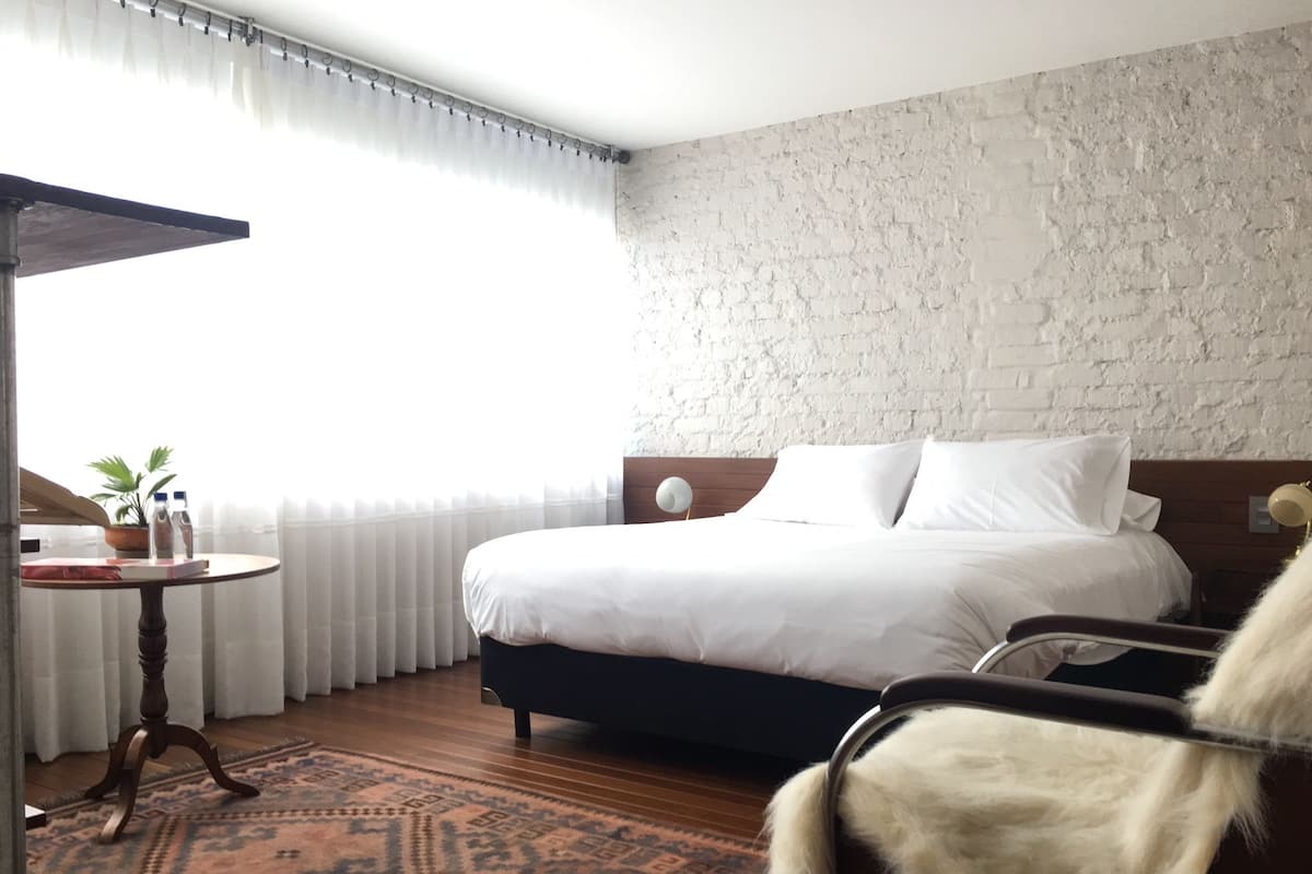 Ein Hotelzimmer mit einem Bett, einem Sessel, einem Tisch mit Pflanze und einem gemusterten Teppich.