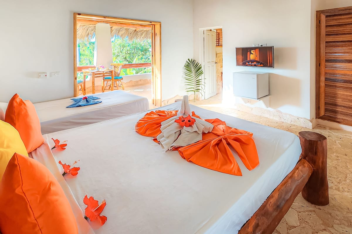 A hotel room with two beds, a TV, and a view of greenery outside.