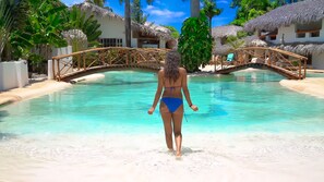 A woman in a blue bikini walking towards a clear pool with a wooden bridge. - Paradiso del Caribe (Las Galeras)