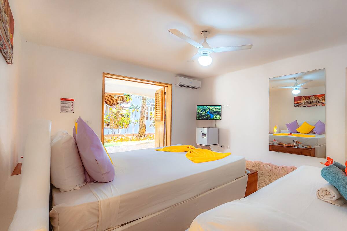 A hotel room with a bed, a TV, a ceiling fan, and a bathroom with a mirror and sink.