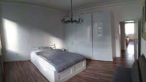 Een slaapkamer met een bed, een garderobe, een kroonluchter en uitzicht op een gang.