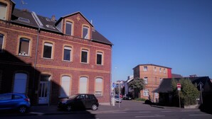 Een straatbeeld met een gebouw van rode baksteen, een blauwe auto en een fietser.