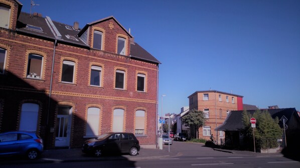 A street view with a red brick building, a blue car, and a cyclist.