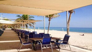 Een café aan het strand met terras onder een zonnescherm, met uitzicht op de oceaan.