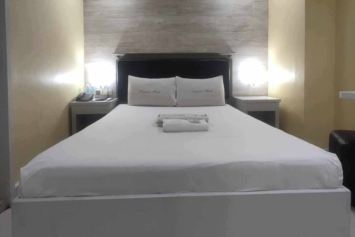 Una habitación de hotel con una cama grande, dos mesitas de noche con lámparas y un cabecero de madera.