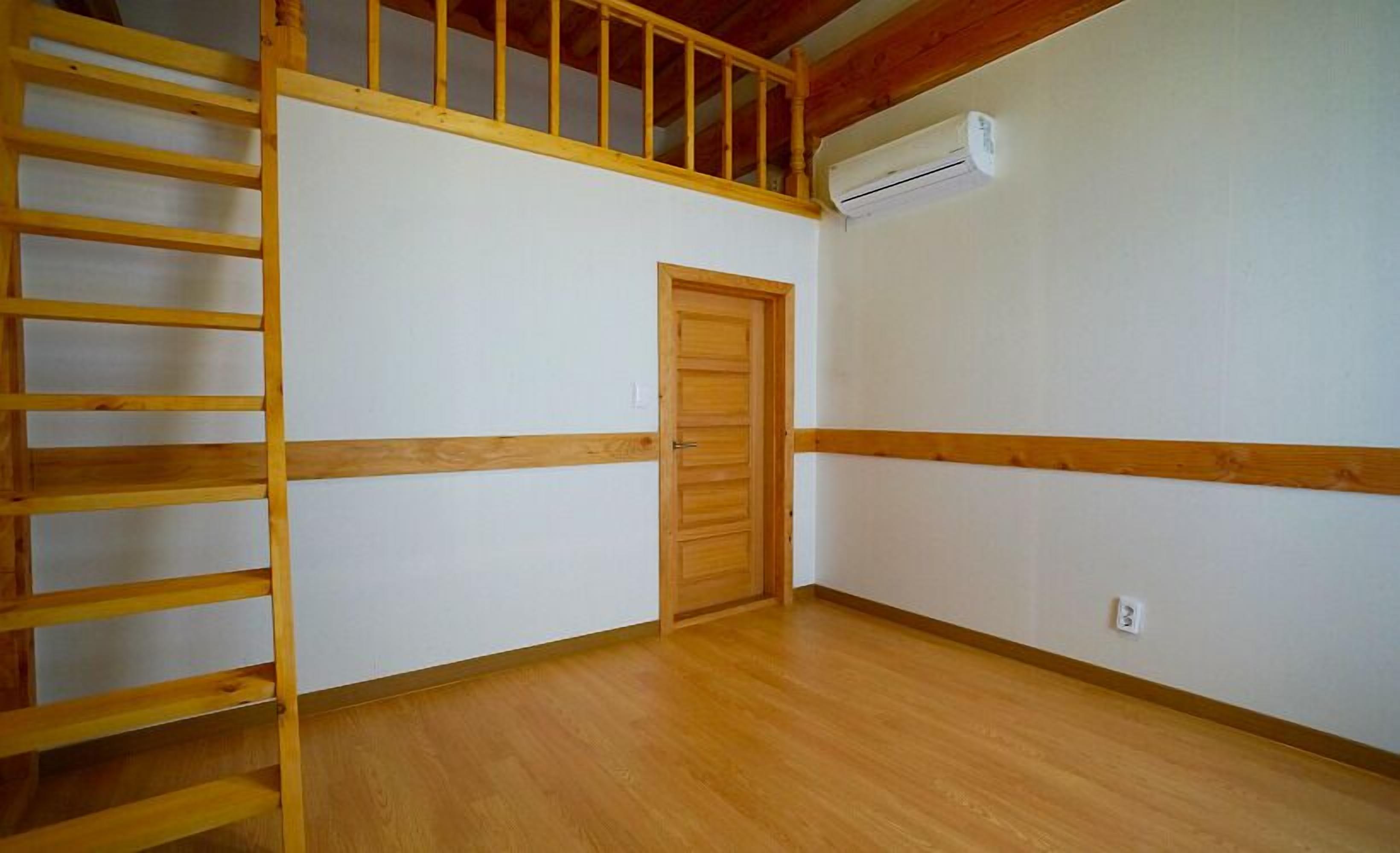 A room with a wooden staircase, a door, and an air conditioning unit on the wall.