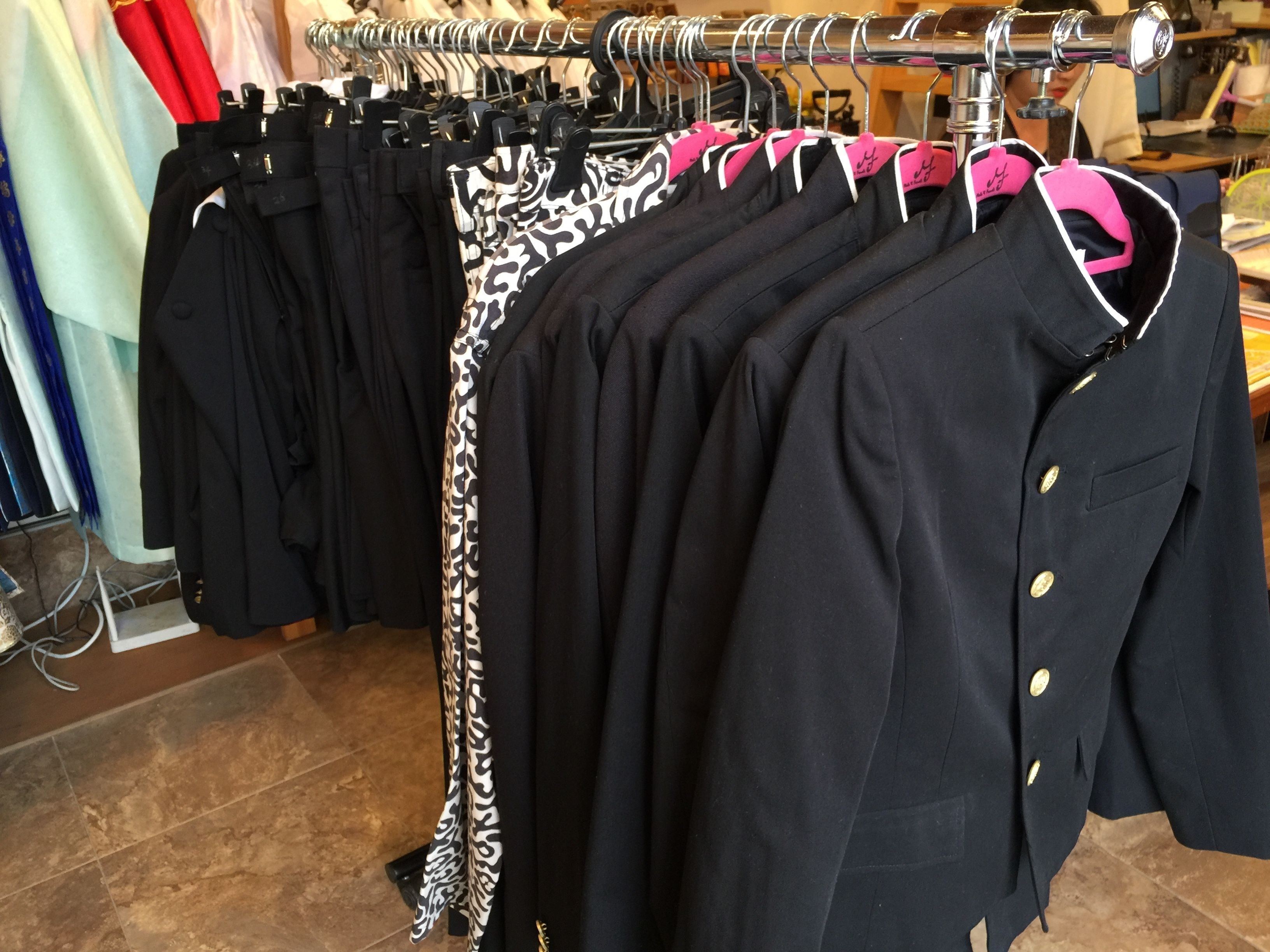 Un portant à vêtements sur lequel sont disposés divers articles, notamment des manteaux noirs et une écharpe à motifs.