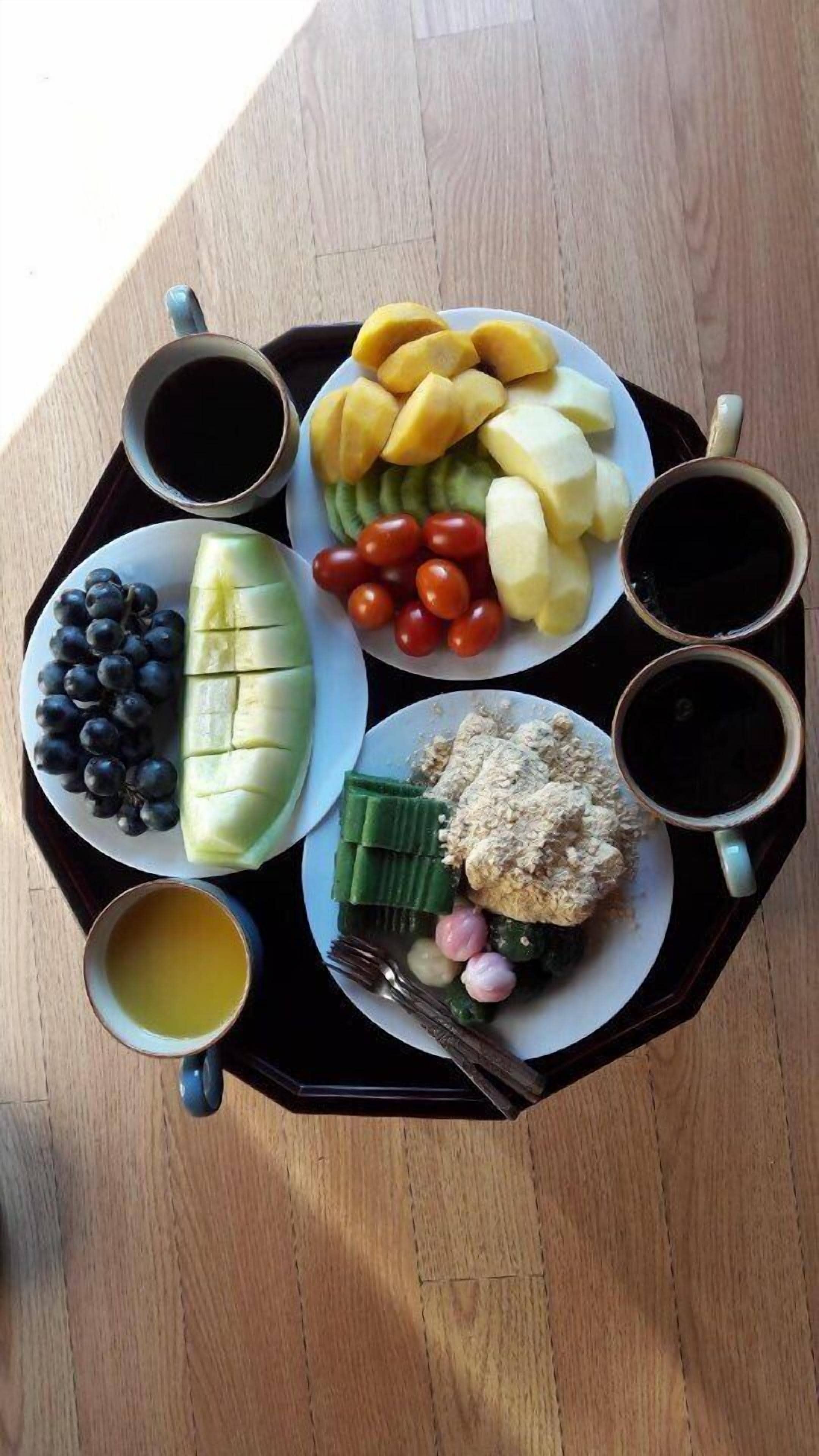A tray with a variety of fruits, vegetables, and beverages, including grapes, mangoes, tomatoes, and a bowl of what appears to be a salad or dip.