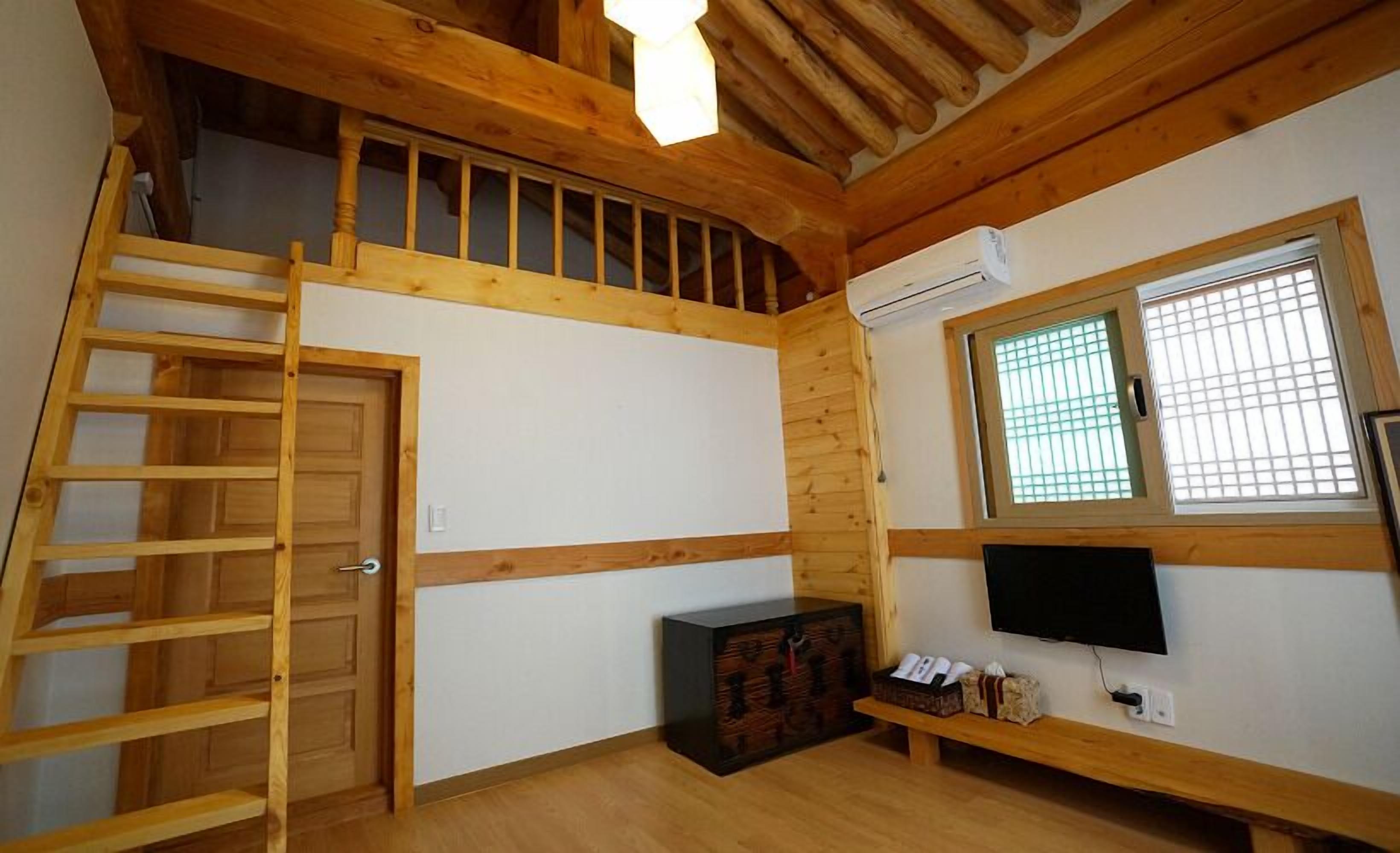 Una habitación con una escalera de madera, un televisor y una ventana con persianas.