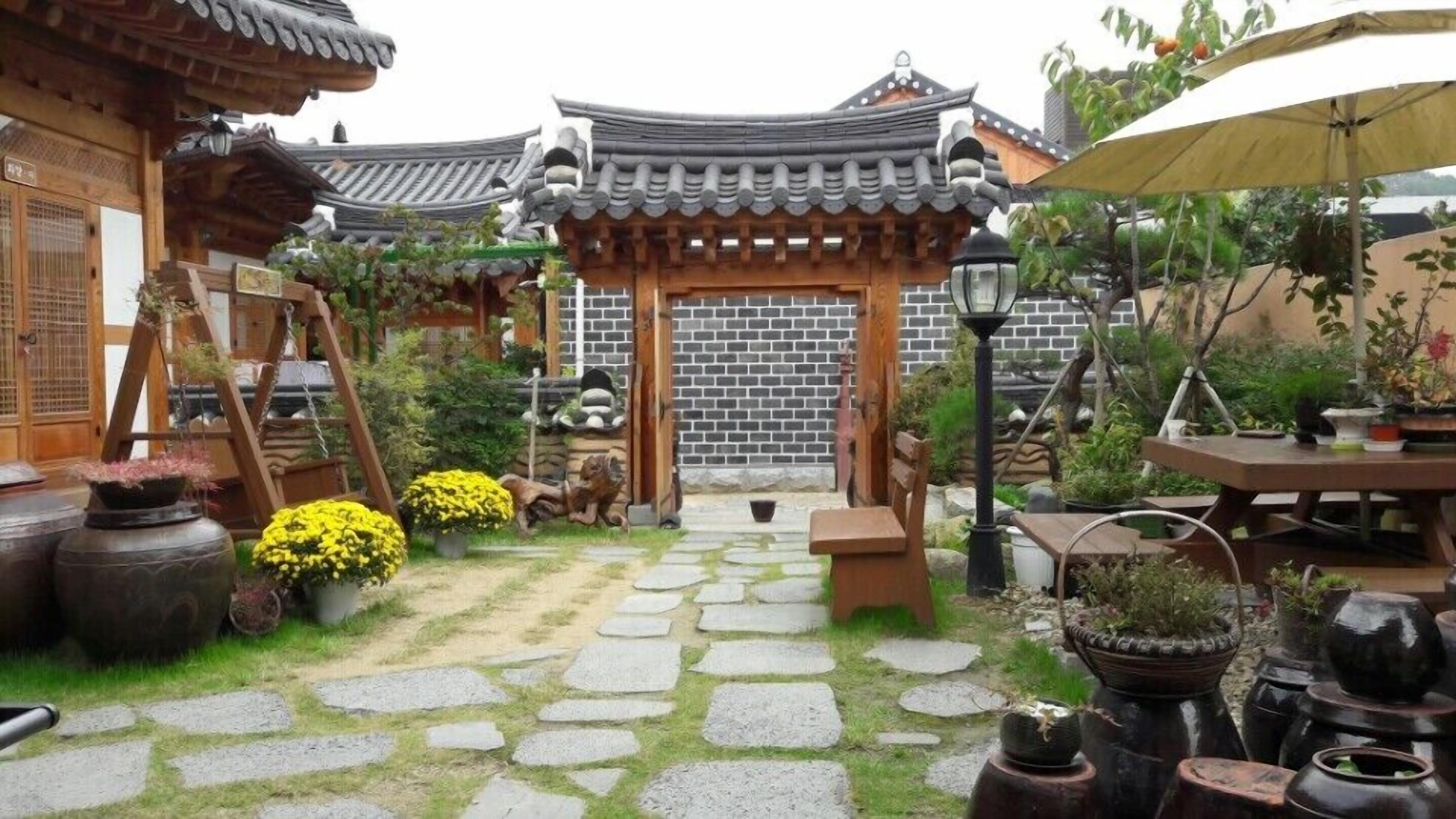 A traditional Korean garden with stone pathways, wooden structures, and potted plants.