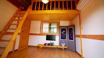 A loft bedroom with a wooden ladder, a TV, a bench, and a window with blinds.