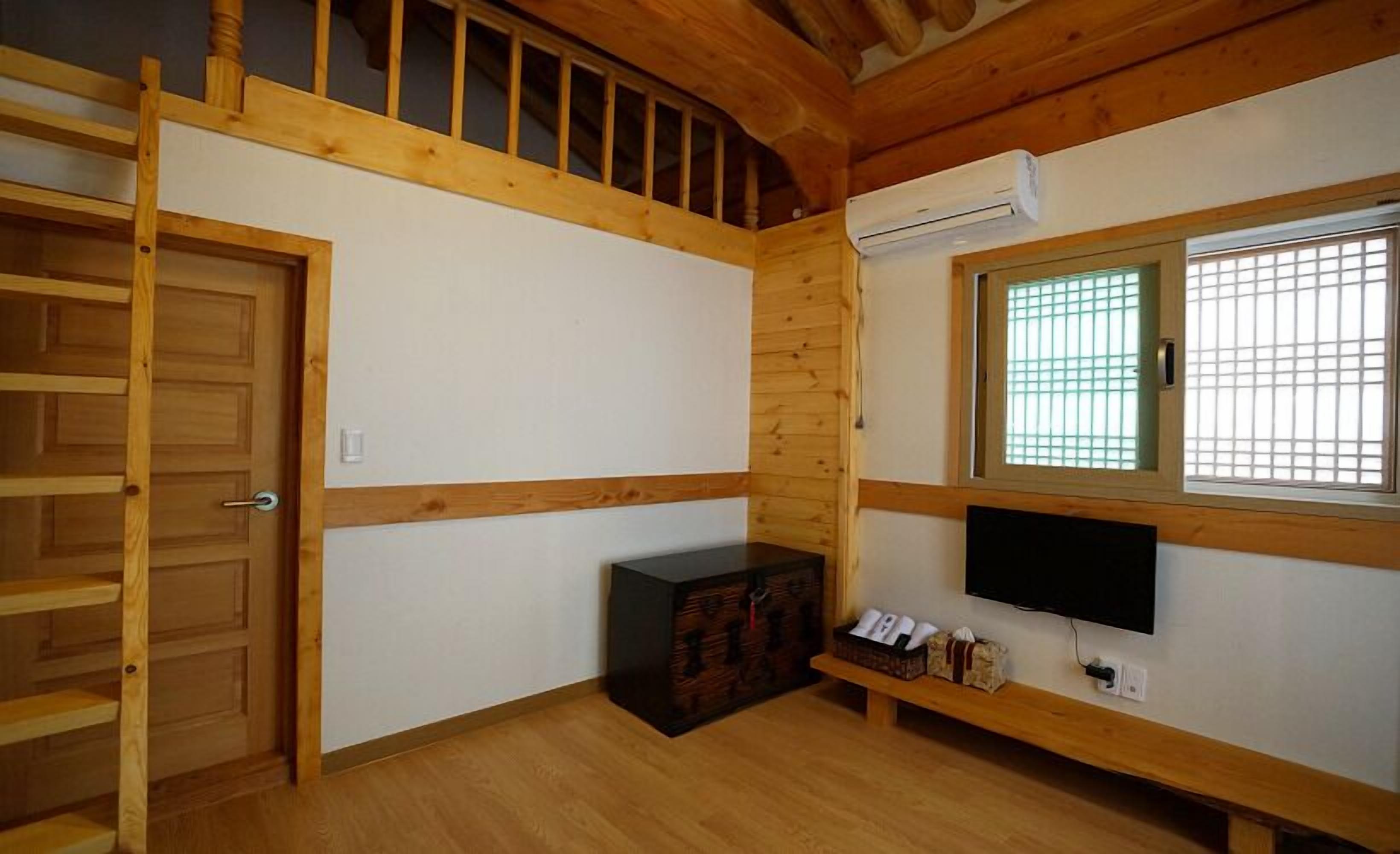 Ein Zimmer mit Holztür, einem fenster mit Gittermuster, einem Fernseher auf einem Holzständer und einem kleinen Schrank mit Gegenständen darin.
