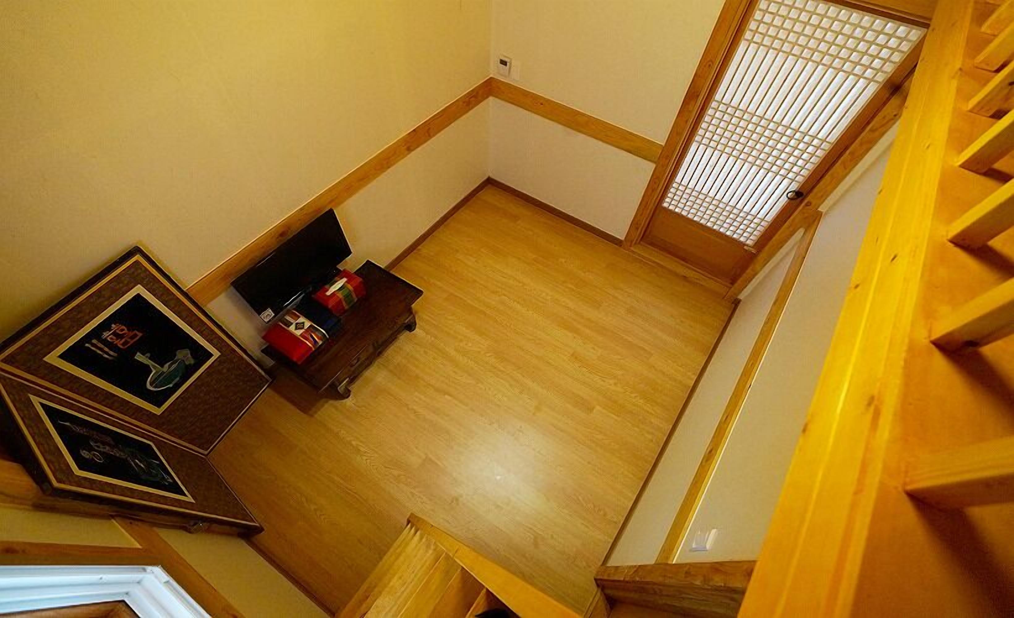 A room with wooden flooring, a small wooden table with items on it, and a corner with a wooden baseboard.