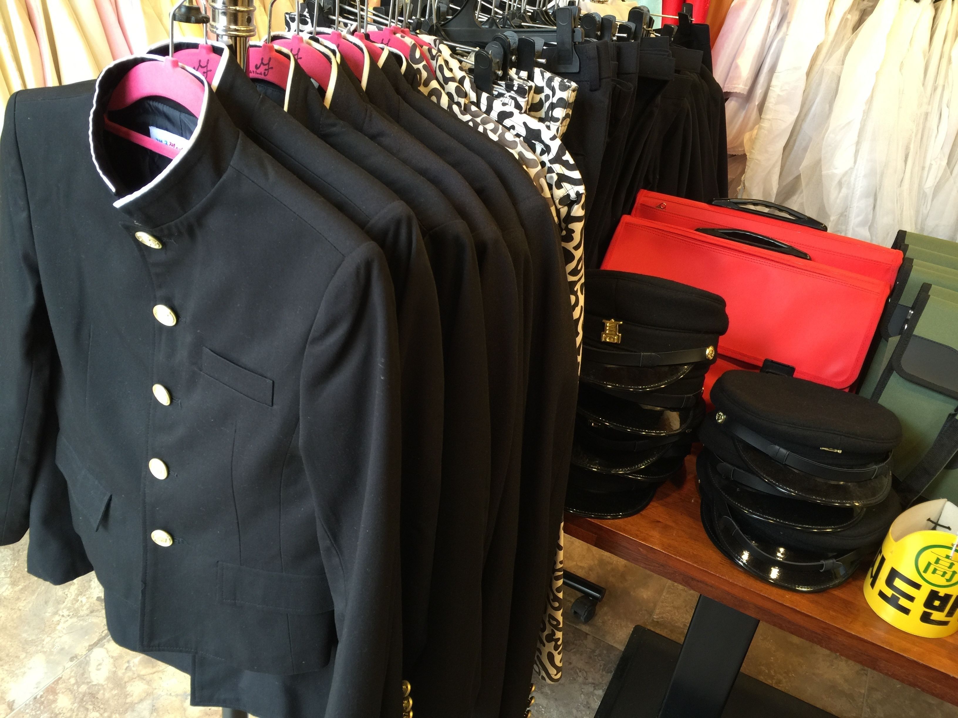 A clothing rack with various garments, including a black jacket with gold buttons, a red bag, and a yellow mug.