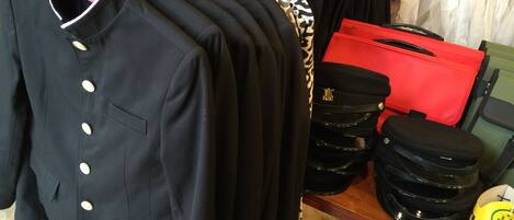 A clothing rack with various garments, including a black jacket with gold buttons, a red bag, and a yellow mug.